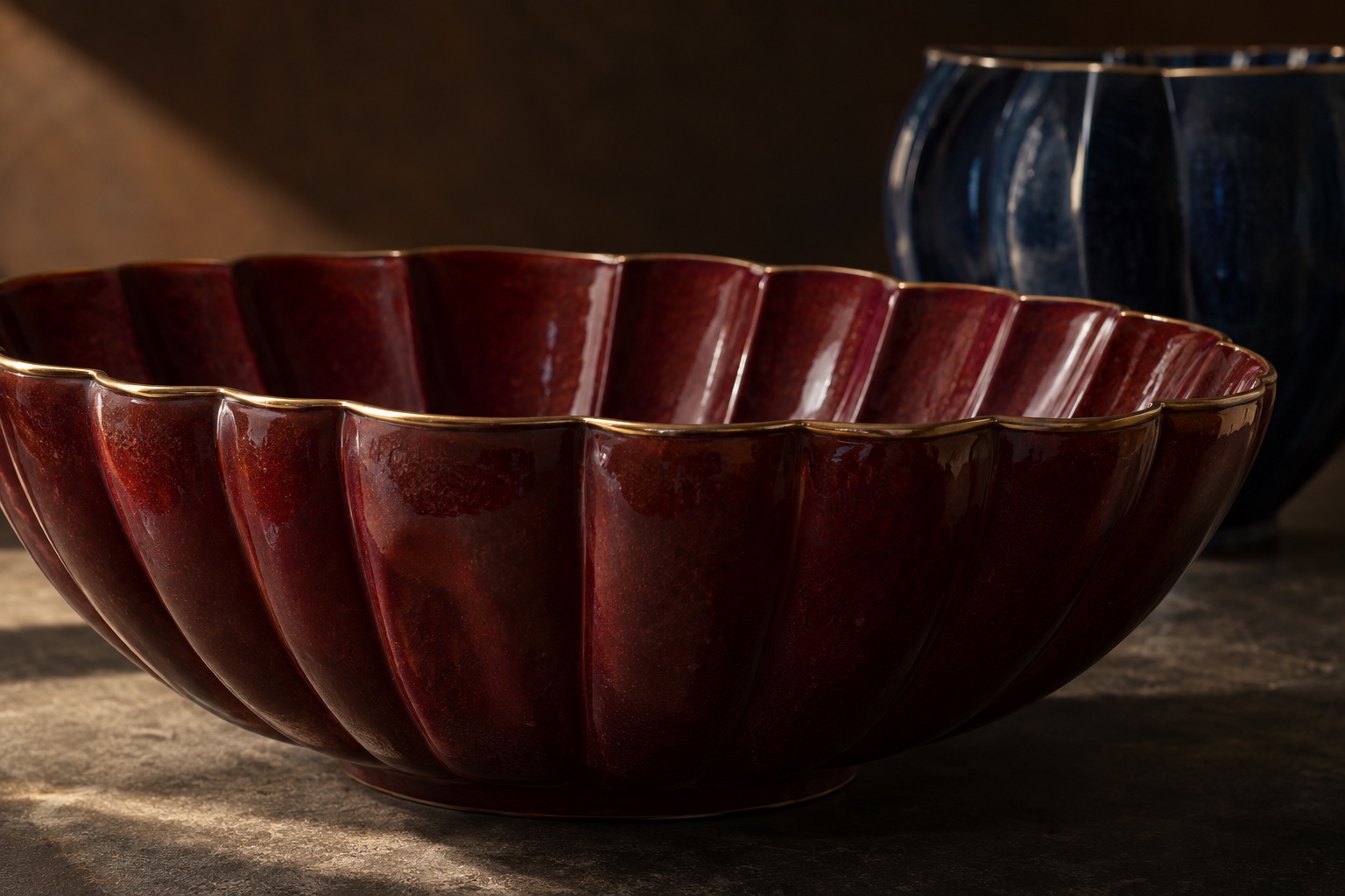 A close view of the sculpted flutes, deep burgundy glaze, and fine gold edge of a handcrafted ceramic bowl.